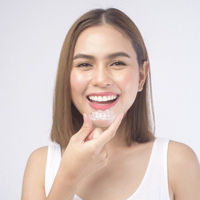 Happy young woman in white t-shirt holding clear aligner