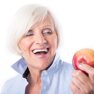 woman about to eat an apple and enjoy the health benefits of dental implants in Burien