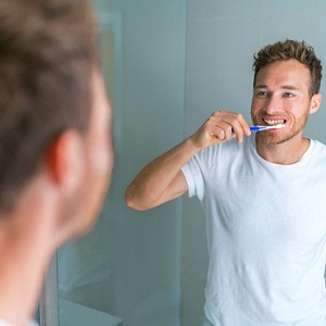 A young man brushing his teeth to keep his dental implants in Burien clean